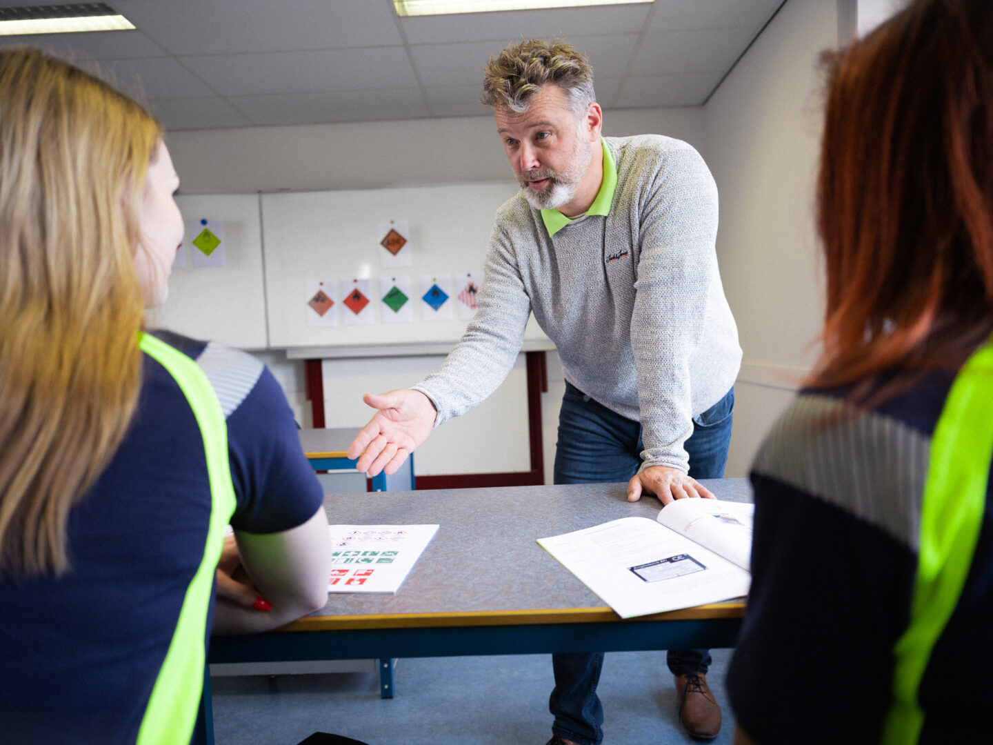 Docent geeft uitleg aan 2 vrouwen met bord op achtergrond